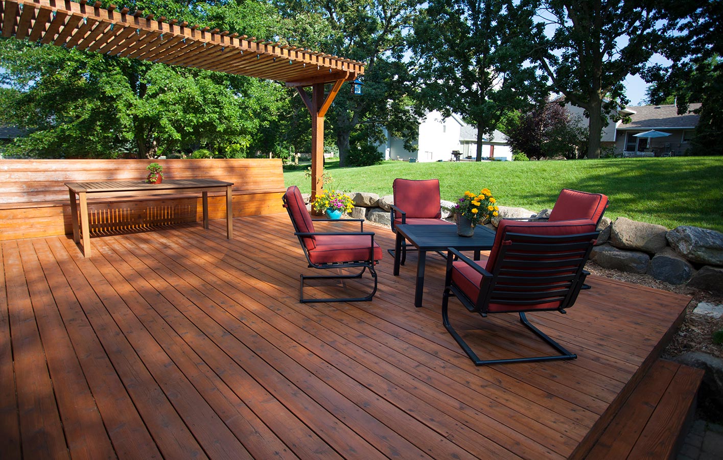 Große dunkelbraune Holzterrasse mit roten Stühlen