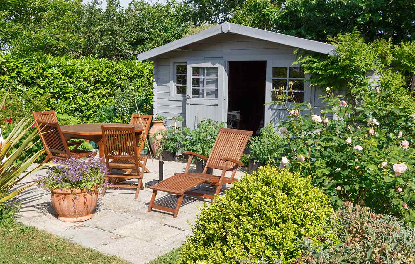 Hellblau gestrichendes Gartenhäuschen aus Holz mit Tisch und Stühlen davor