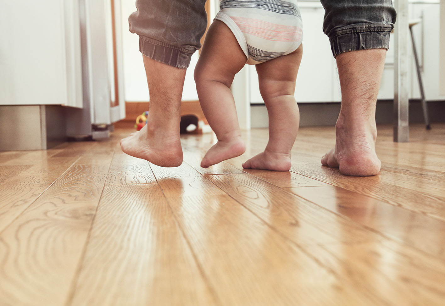 Die Füße von einem Vater mit seinem Kind auf einem Echtholzfußboden