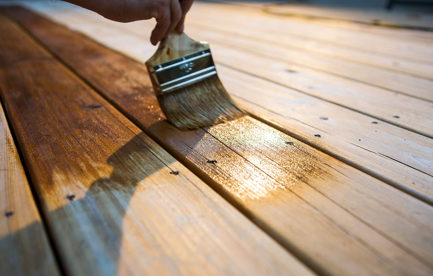 Eine Hand Streicht mit dem Oinsel über Terrassendielen aus Holz