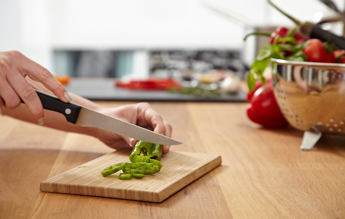 Eine Hand schneidt Gemüse auf einer Küchenplatte aus Holz