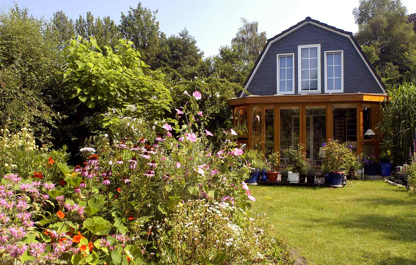 Ein Garten mit Blumen vor einem Haus mit einer überdachten Holzterrasse